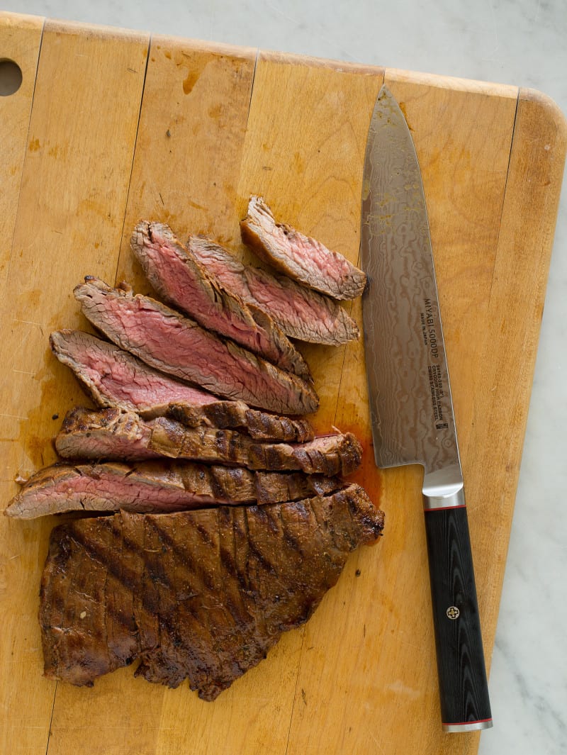 A knife sitting on top of a wooden cutting board with carne asada.