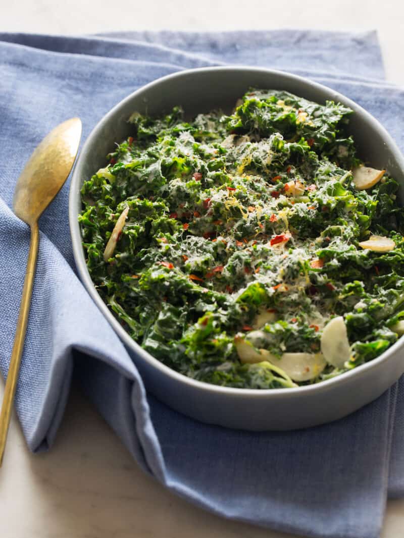 A serving dish of creamed kale with a blue napkin and a spoon.