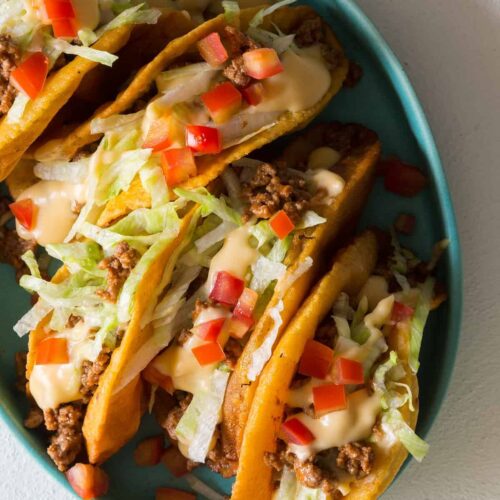 A plate of crunchy beef tacos with a cheese sauce on top.