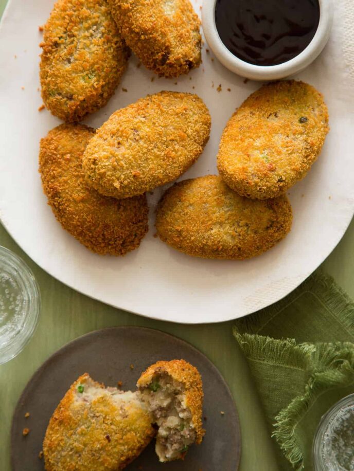 A close up of korokke on a plate next to sauce.