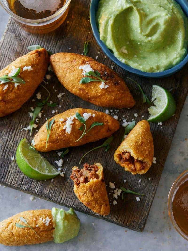 A close up of chorizo molotes with creamy avocado dipping sauce and lime wedges.