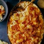 Cheesy potatoes with caramelized onions in a pan served with a spoon.