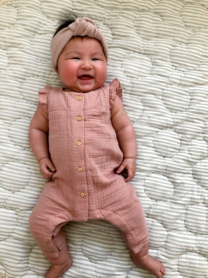 An adorable baby girl in a pink onesie with matching headband laying on a blanket.