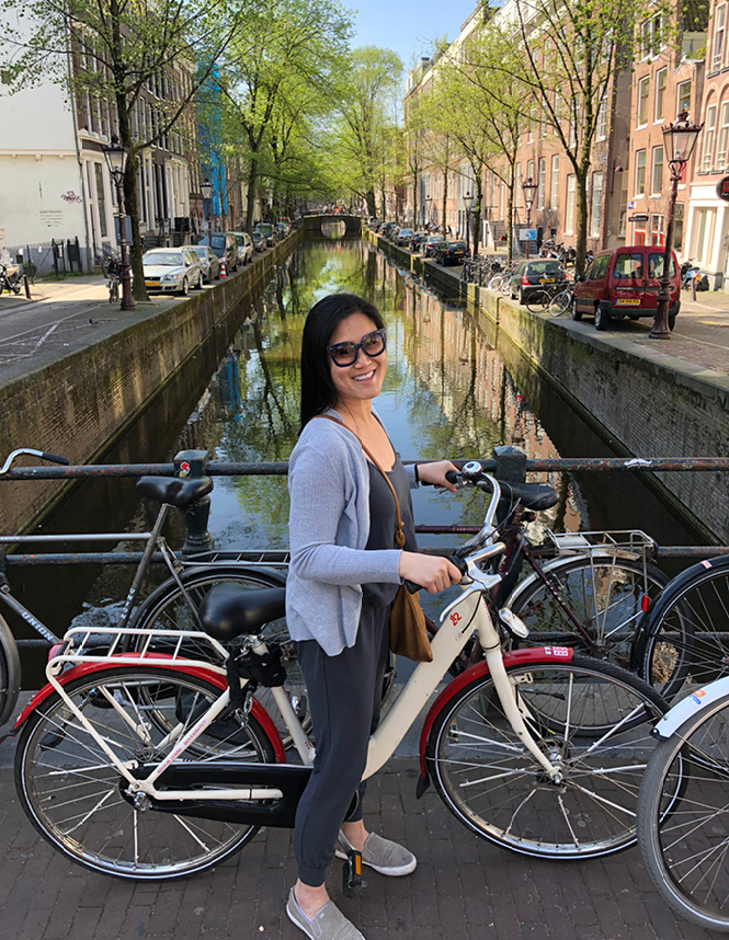 A lovely woman standing on a bicycle in front of a city canal.