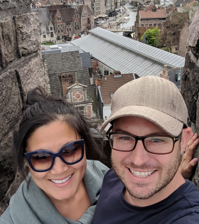 A selfie of a happy couple with buildings in the background.