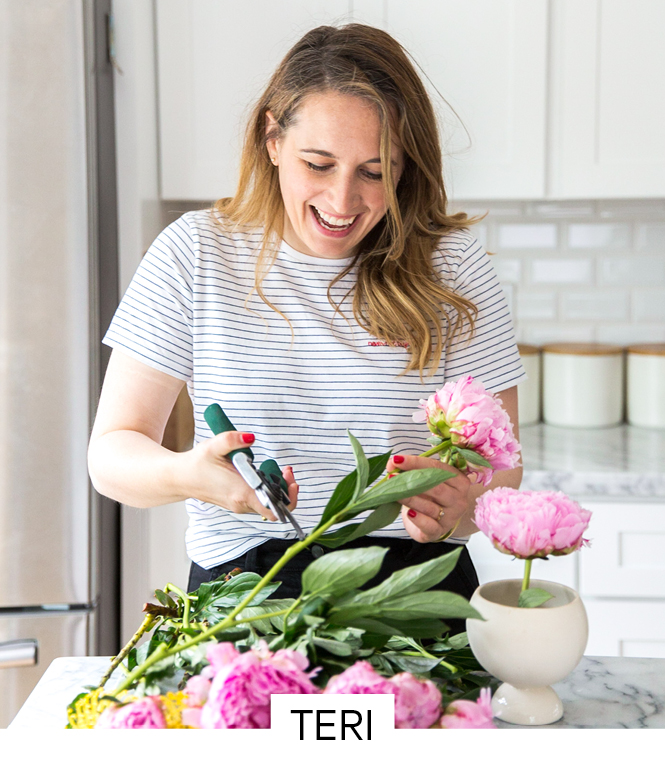 An energetic woman trimming flowers to put in a vase on the countertop.