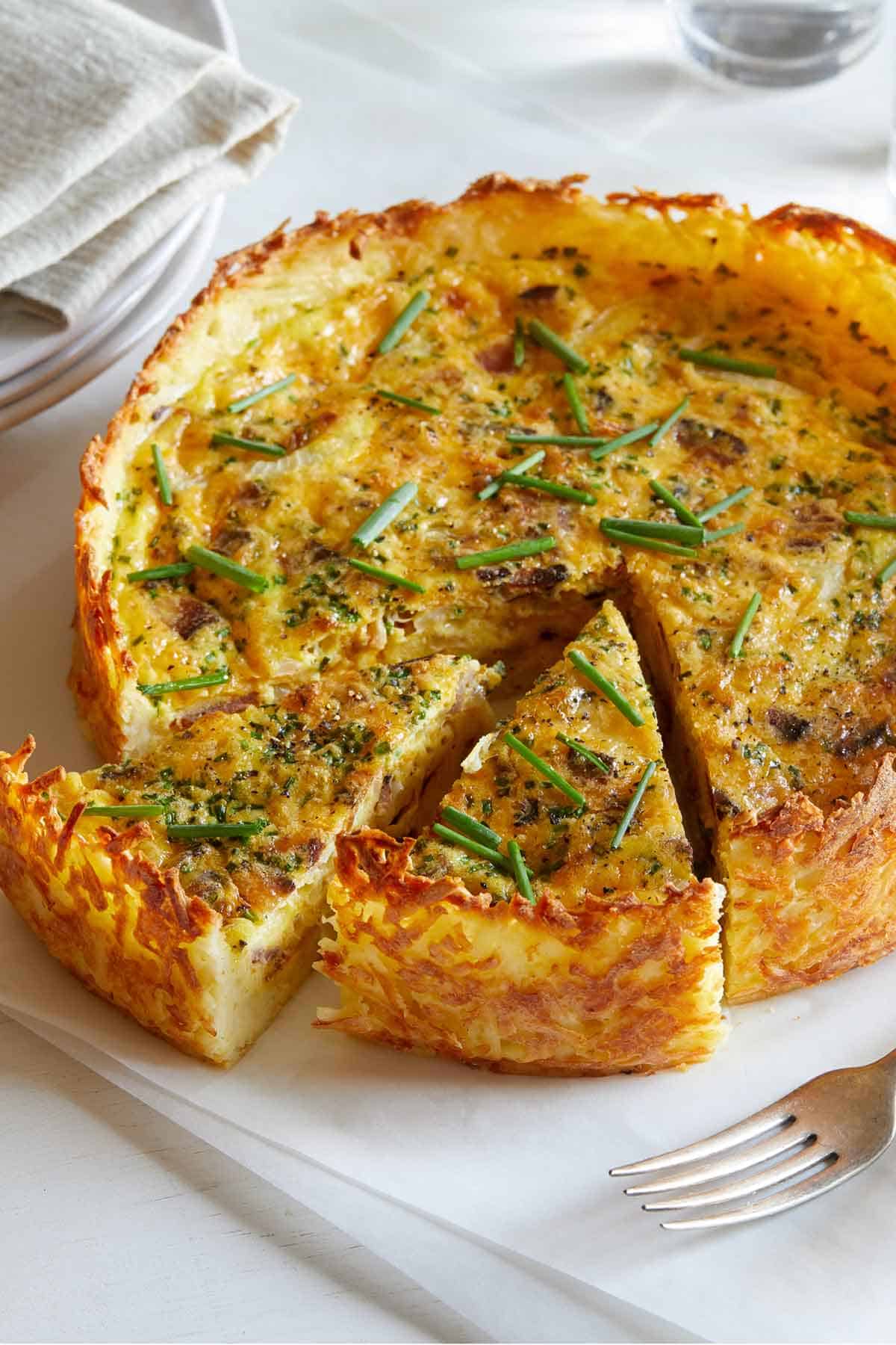 Hash brown quiche with two slices taken out with chives on top.