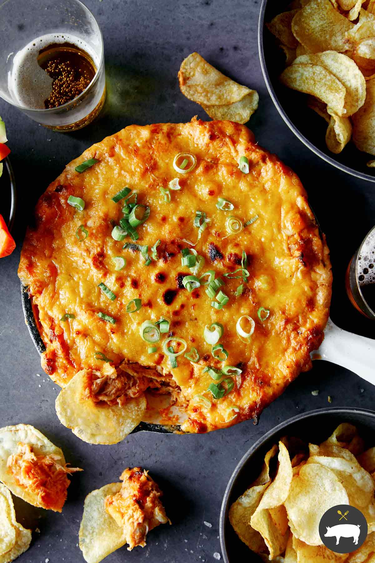 Buffalo chicken dip in a skillet with chips and veggies on the side.