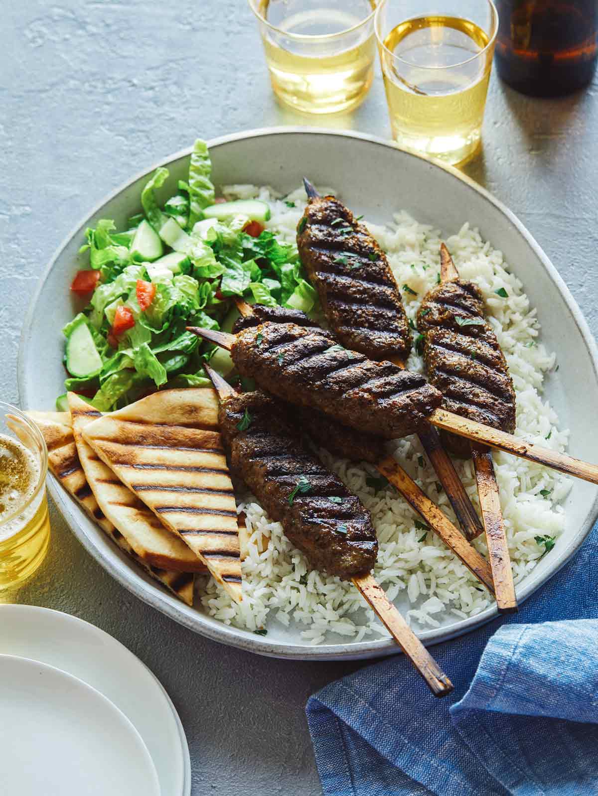 Lamb kofta skewers on a platter with pita and rice.