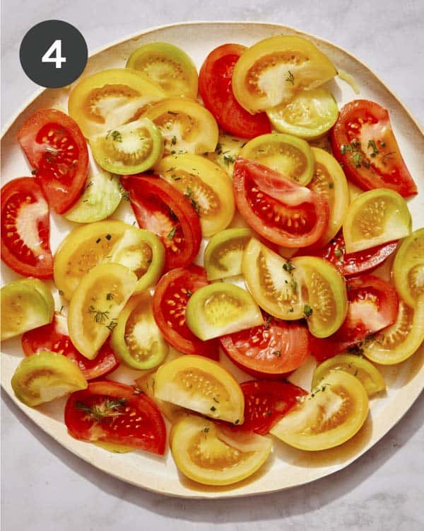 Quartered tomatoes on a plate with herbs. 