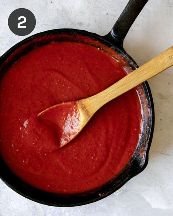 Blended ingredients to make a red sauce simmering in  a skillet. 