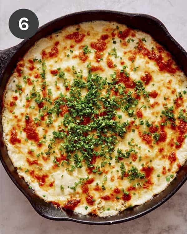 Crab dip baked in a skillet with chives on top.
