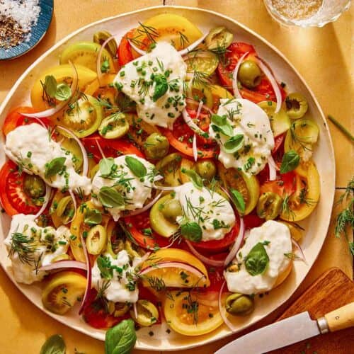 Tomato salad on a plate with herbs on the side.