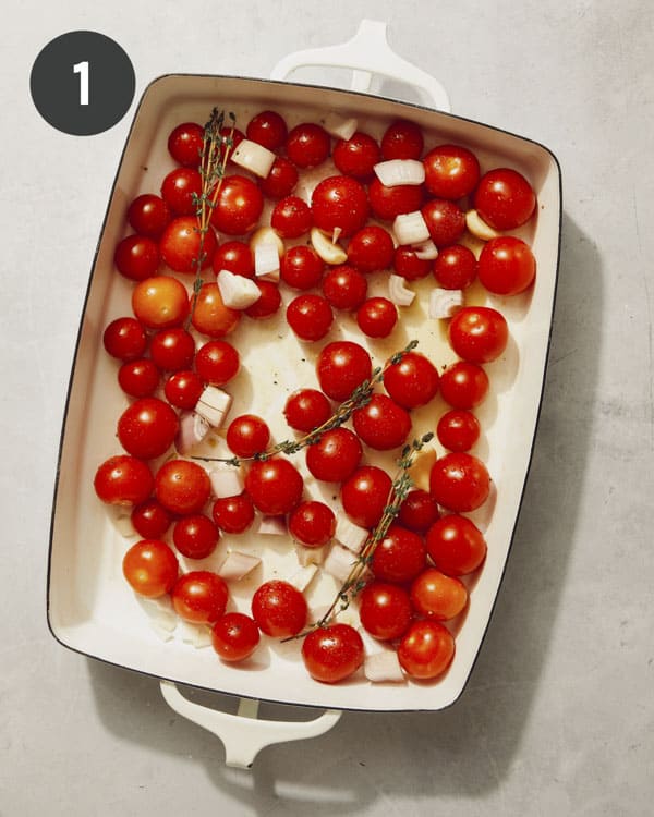 Cherry tomatoes in a baking dish with herbs and butter ready to be roasted. 