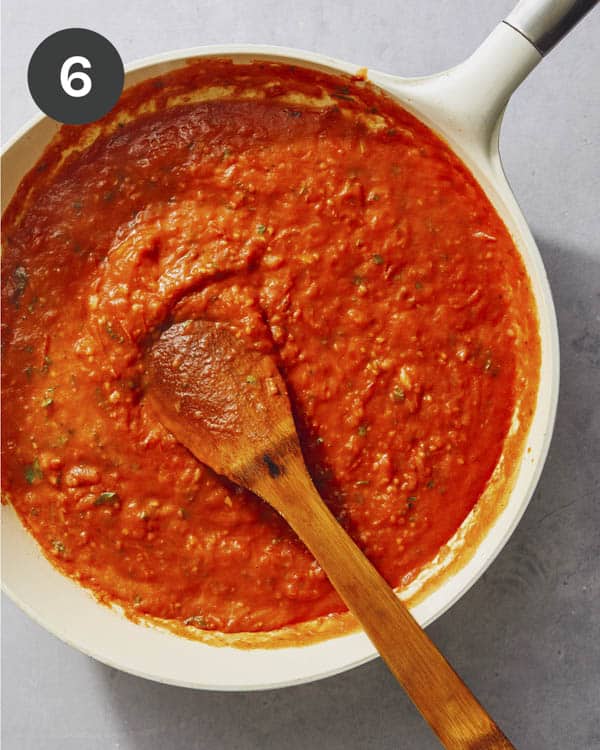 Tomato sauce in a skillet with a wood spoon being simmered.