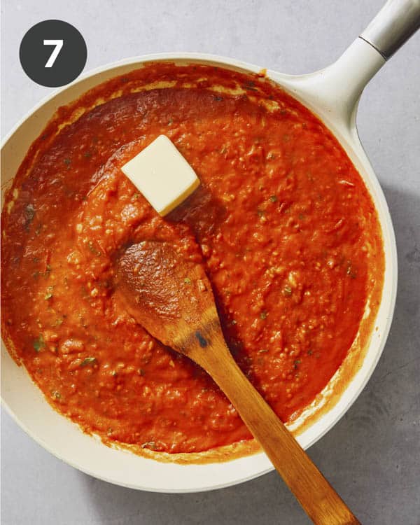 Tomato sauce in a skillet being cooked down with butter being added.