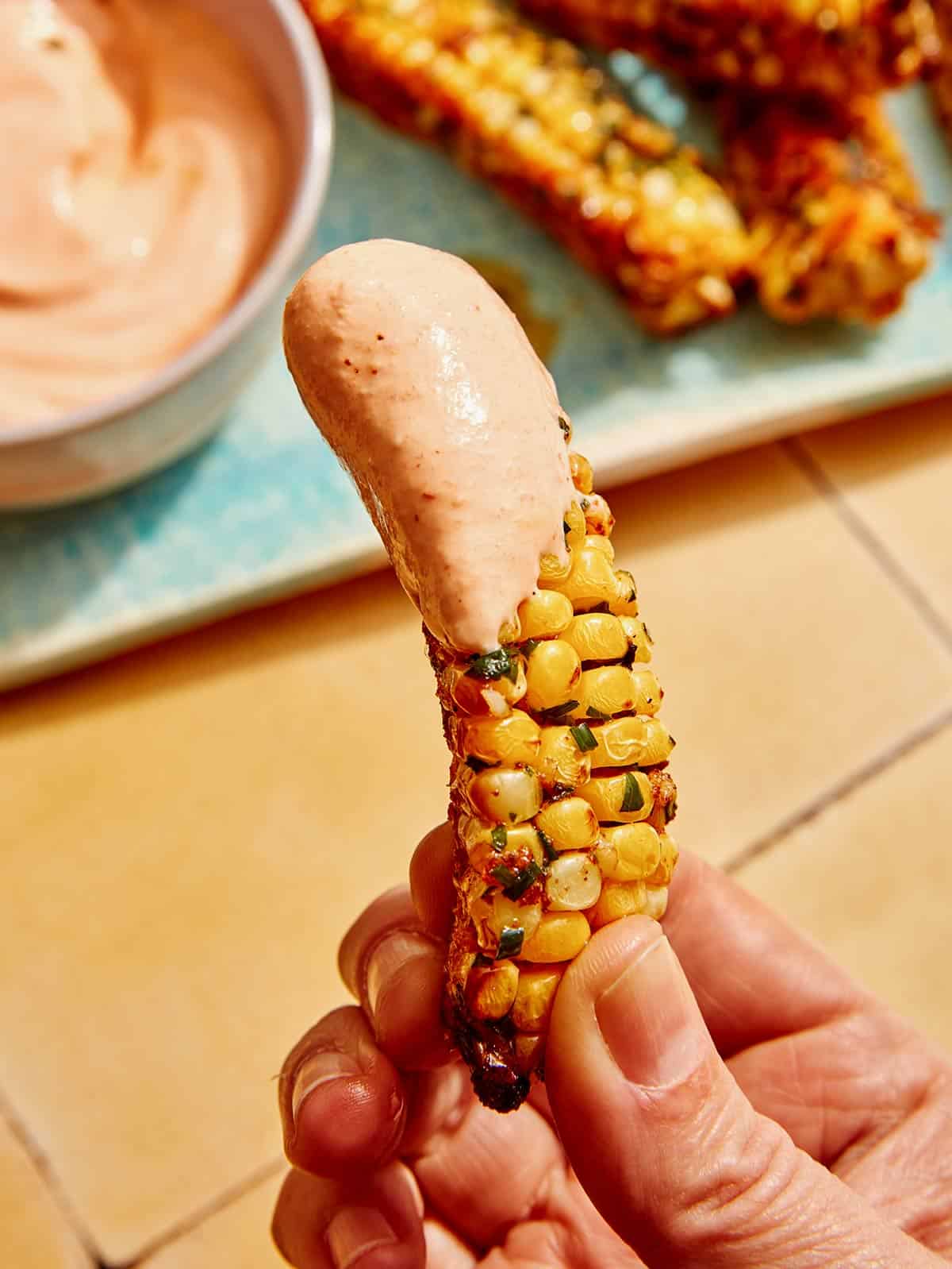 A hand holding an air fryer corn rib with sauce on it.