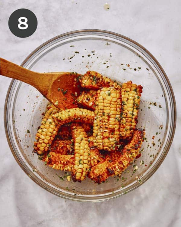 Corn ribs in a glass bowl being tossed with an herbed butter.