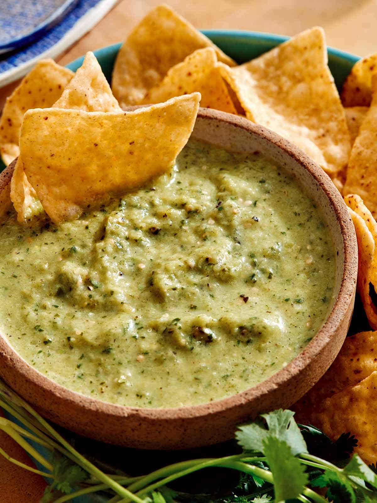 Tomatillo salsa in a bowl with chips being served on the side.