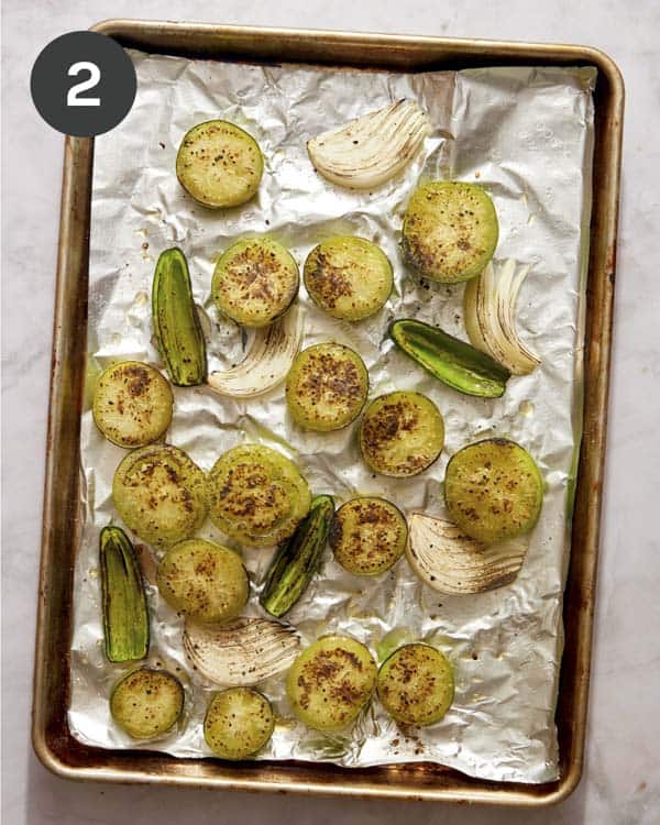 Tomatillo salsa ingredients on a baking sheet after they have been roasted. 