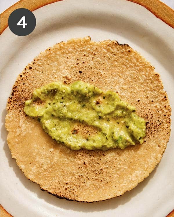 A corn tortilla on a plate with tomatillo salsa smeared on it.