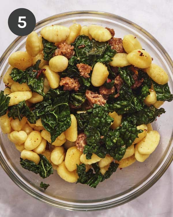 Gnocchi added to a bowl with sausage and kale. 