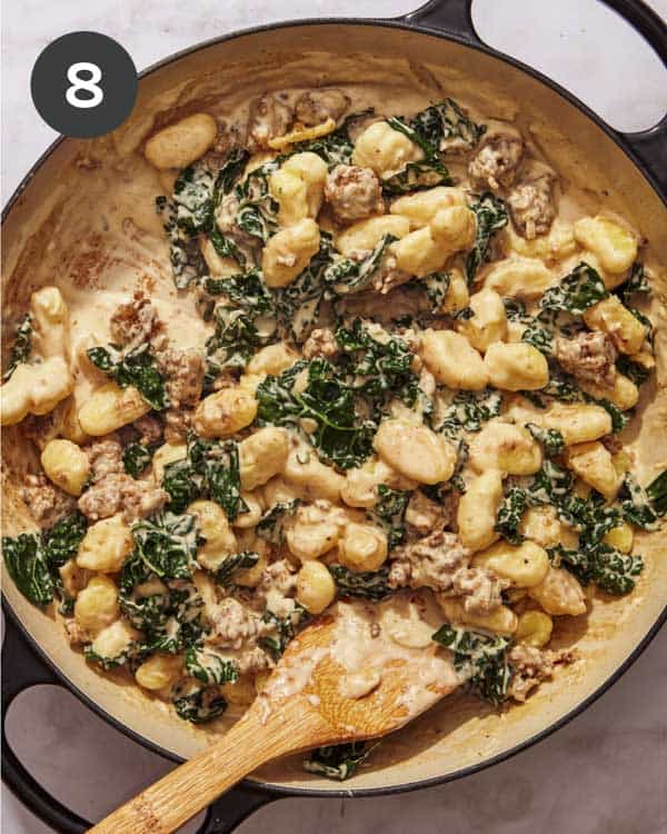 Gnocchi, kale, and sausage in a skillet being tossed with a cream sauce.