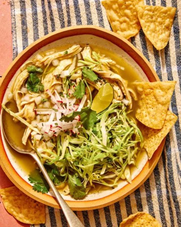 Chicken pozole verde in a bowl with chips on the side.