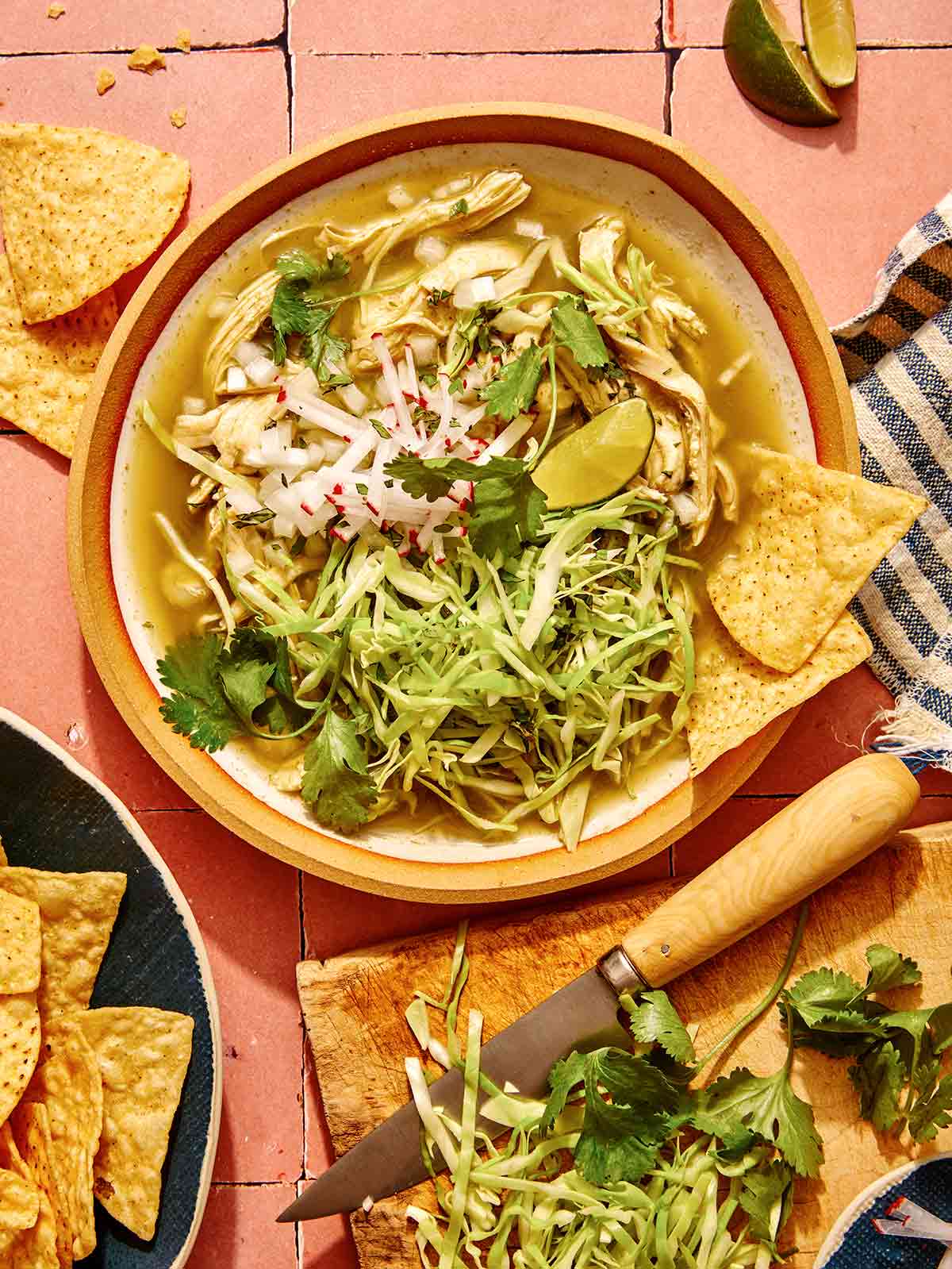 Chicken pozole verde in a bowl with garnishes and chips on the side.