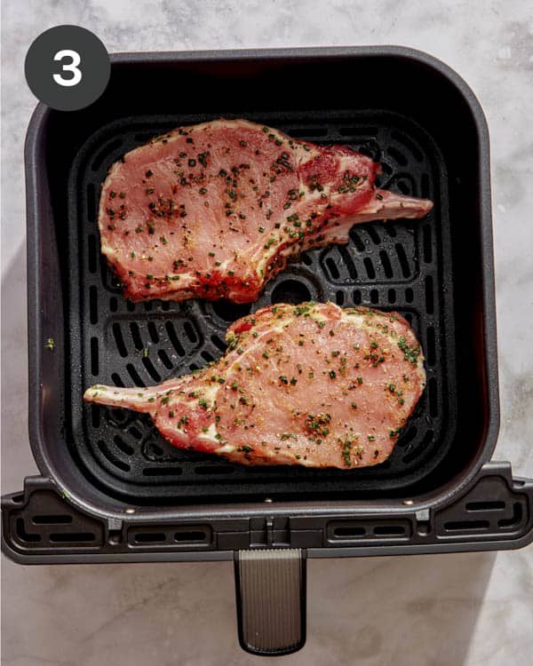 Pork chops in an air fryer basket about to be air fried. 