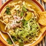 Chicken pozole verde in a bowl with chips on the side.